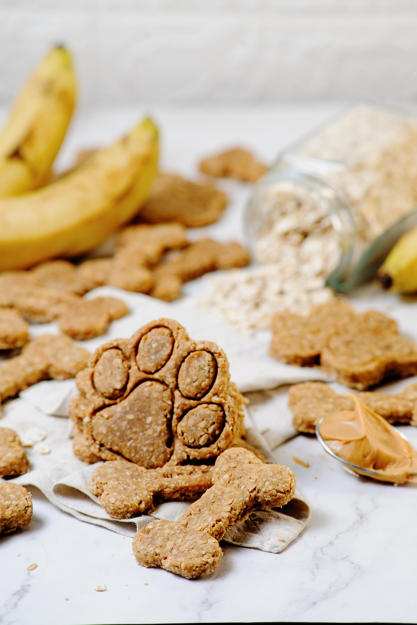 Peanut Butter and Banana Cookies in the shape of a dog paw print with bananas and rolled oats in the background